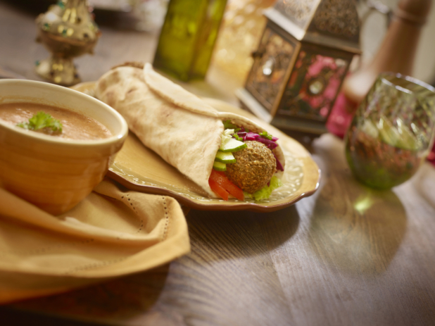Falafel Pita Wrap with Pickled Veggies and Fresh Vegetables on a Coloured Ceramic Dish with a Bowl of Thick Hot Vegetarian Soup on a Wooden Table in an Indoor Setting
