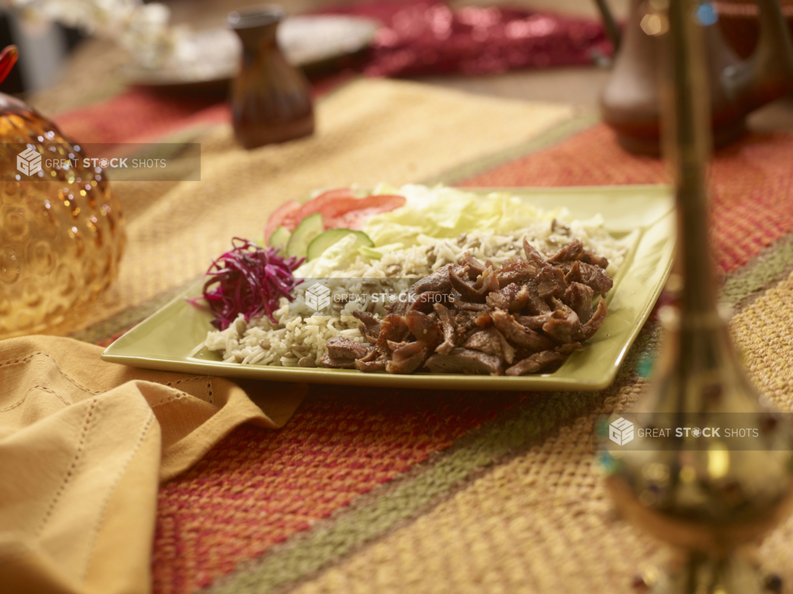 Combo Meal of Beef Shawarma with a Garden Salad, Picked Veggies, Rice and Lentils in a Ceramic Dish on a Woven Placemat in an Indoor Setting