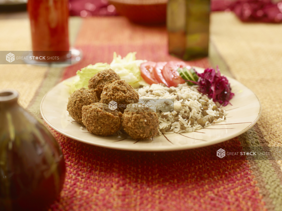 Vegetarian Combo Meal of Falafel Balls with a Garden Salad, Picked Veggies, Rice and Lentils in a Ceramic Dish on a Woven Placemat in an Indoor Setting