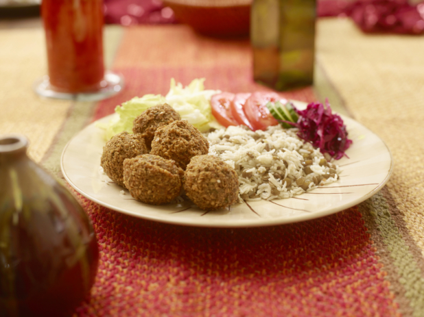 Vegetarian Combo Meal of Falafel Balls with a Garden Salad, Picked Veggies, Rice and Lentils in a Ceramic Dish on a Woven Placemat in an Indoor Setting