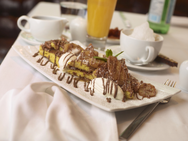 Chocolate Banana French Toast with Whipped Cream and Powdered Sugar and Other Breakfast Items on a White Table Cloth Table Setting