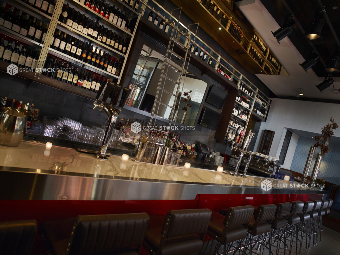 Bar Counter and Bar Stools with Backs and a Wall Lined with Bottles of Wine and a Ladder in a Casual Restaurant Setting