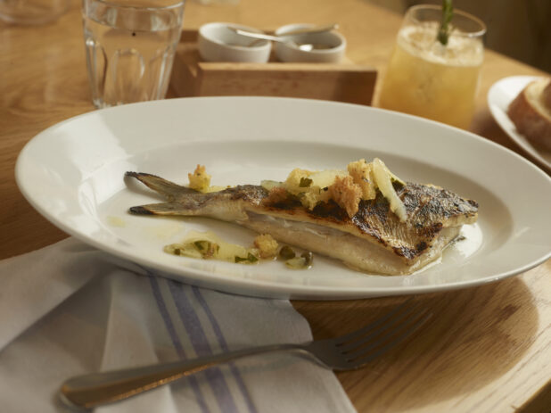 Orata (Gilt-head Bream) with Capers, Mint and Toasted Focaccia on a Round White Plate on a Wooden Table in a Casual Dining Setting