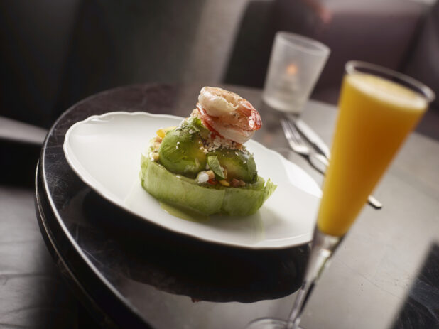 Shrimp and Avocado Wedge Salad on a Round White Plate with a Mimosa Cocktail on a Round Dark Wood Table in a Restaurant Setting