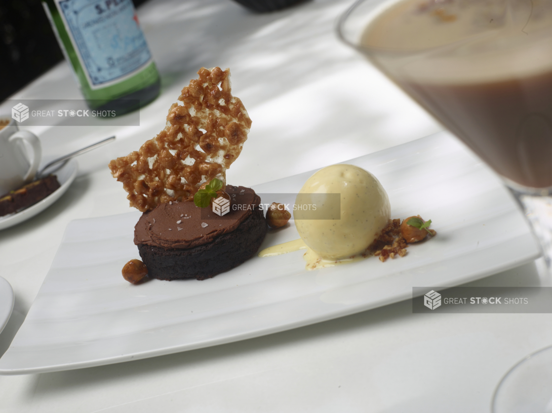 Dessert Platter of Chocolate Gateau with Nut Brittle and French Vanilla Ice Cream on a White Rectangular Dish on a White Table Cloth in an Outdoor Dining Setting