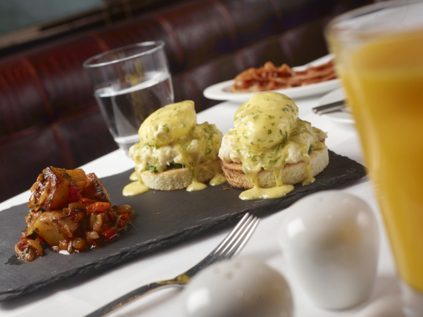 Eggs Benedict with a Side of Roasted Potatoes and Vegetables and Other Breakfast Items on a White Table Cloth Table Setting