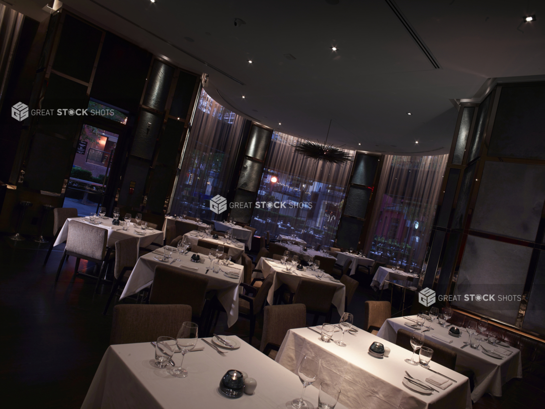 Classy Restaurant Interior with Dark, Moody Lighting, Formal Table Settings and a Semi-Circular Seating Area with Floor to Ceiling Windows