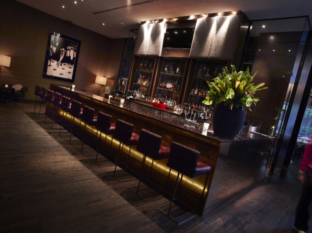 Bar Lounge Area in a Classy, High-End Restaurant Interior with Dark Wood Flooring, Moody Lighting and Red Leather Bar Stools