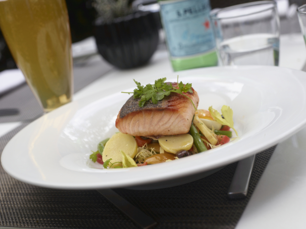 Pan-Seared Salmon Fillet on a Bed of Golden Beet, Frisée, Tomatoes and Green Beans in a Round White Dish on a Placemat in an Outdoor Dining Setting
