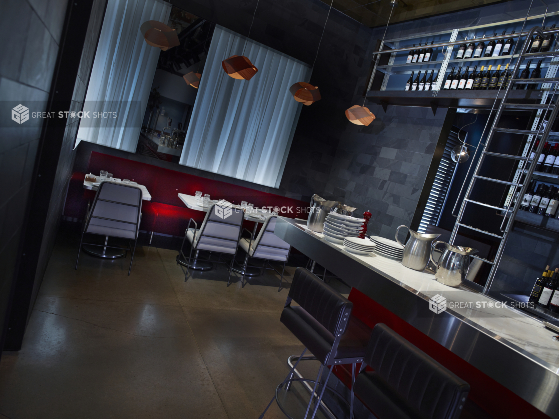 Bar Counter and Cozy Seating Area of a Casual Restaurant Interior with Bottles of Wine and Red Cushioned Seating Along the Walls