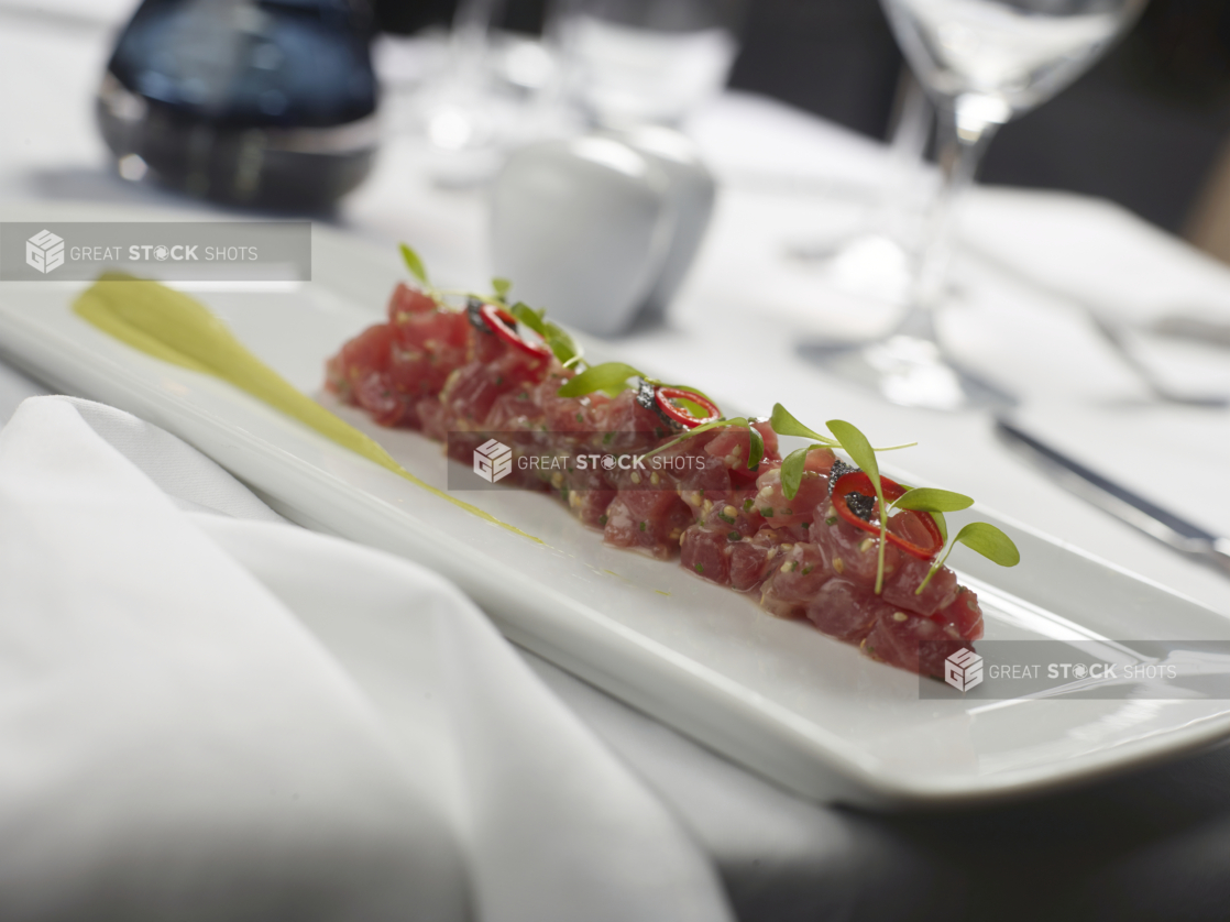 Ahi Tuna Tartare with Microgreens, Yuzu Dressing and Avocado Purée on a White Rectangular Platter on a White Table Cloth Table Setting