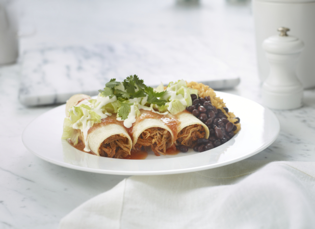 Meat enchiladas with black beans and rice on a white plate on a white marble background