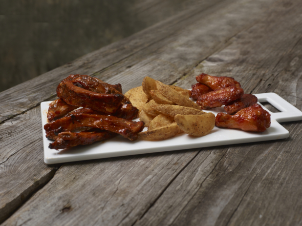 A White Rectangular Ceramic Platter with BBQ Ribs, Potato Wedges and BBQ Chicken Wings on an Aged Wooden Surface