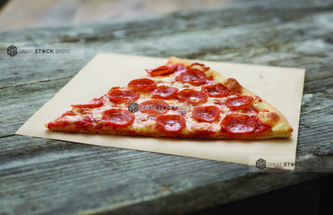 Jumbo Slice of Pepperoni Pizza on Parchment Paper on an Aged Wood Background