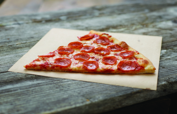 Jumbo Slice of Pepperoni Pizza on Parchment Paper on an Aged Wood Background