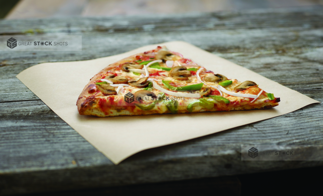 Jumbo Slice of Vegetarian Pizza with Mushrooms, Green Peppers and Onions on Parchment Paper on an Aged Wood Background