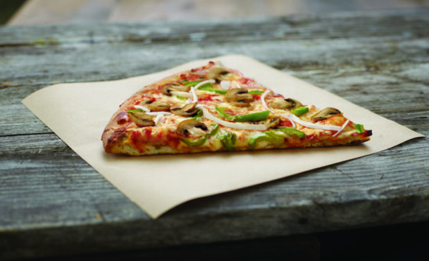 Jumbo Slice of Vegetarian Pizza with Mushrooms, Green Peppers and Onions on Parchment Paper on an Aged Wood Background