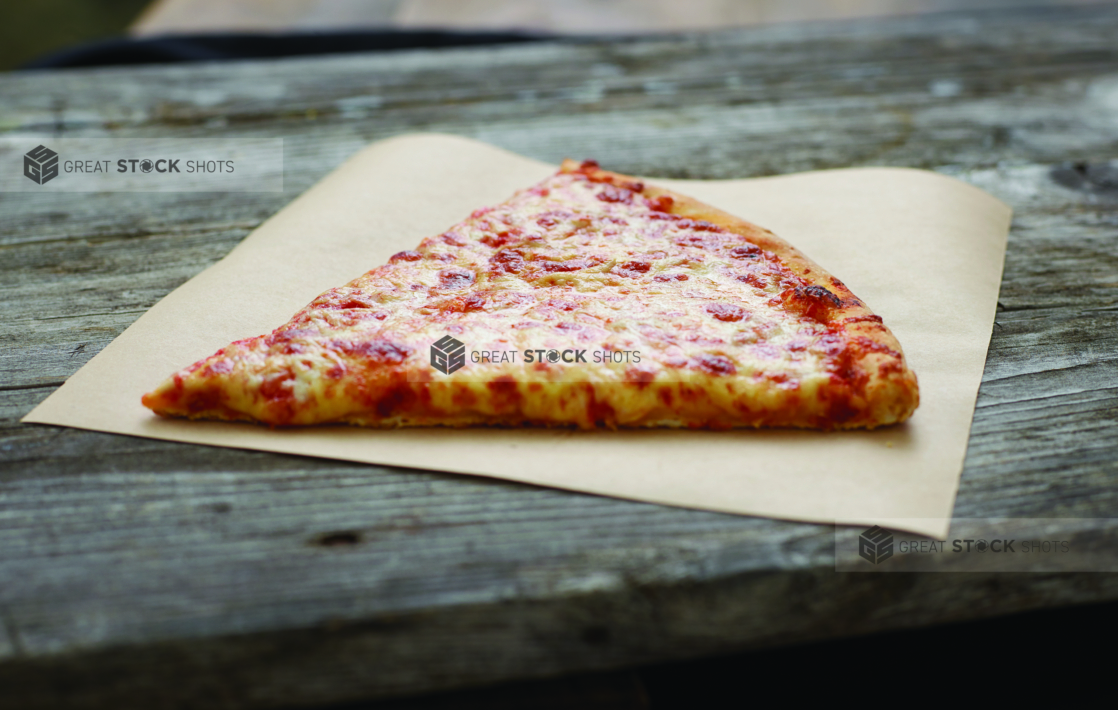 A Jumbo Slice of Cheese Pizza on Parchment Paper on an Aged Wood Background