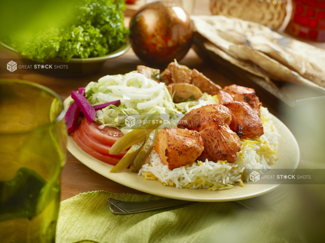 BBQ Chicken Kebab Combo Dinner with a Garden Salad, Roasted Garlic Potatoes, Picked Veggies and White Rice in a Ceramic Dish on a Wooden Table in an Indoor Setting