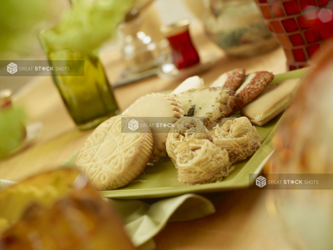 Assorted Middle Eastern Cookies and Sweets - Maamoul, Kahk-Eid, Ghreybeh and Kataifi - on a Round Ceramic Dish on a Wooden Table in an Indoor Setting