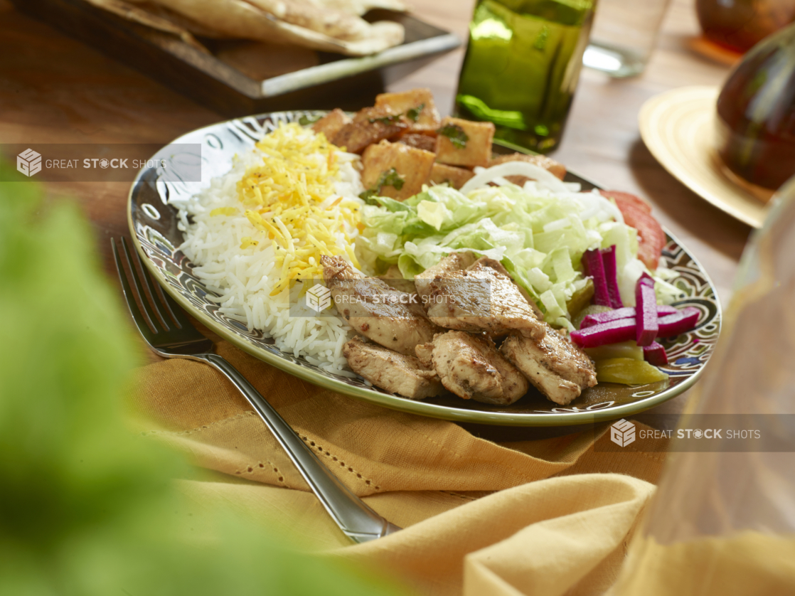 Chicken Souvlaki Combo Dinner with a Garden Salad, Roasted Garlic Potatoes, Picked Veggies and White Rice in a Ceramic Dish on a Wooden Table in an Indoor Setting