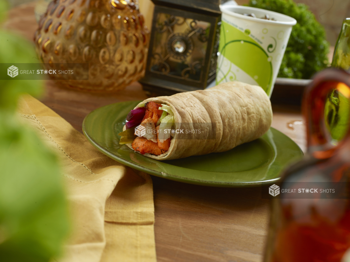 BBQ Chicken Kebab Pita Wrap with Pickled Veggies and Fresh Vegetables on a Round Ceramic Dish with a Fountain Soda on a Wooden Table in an Indoor Setting