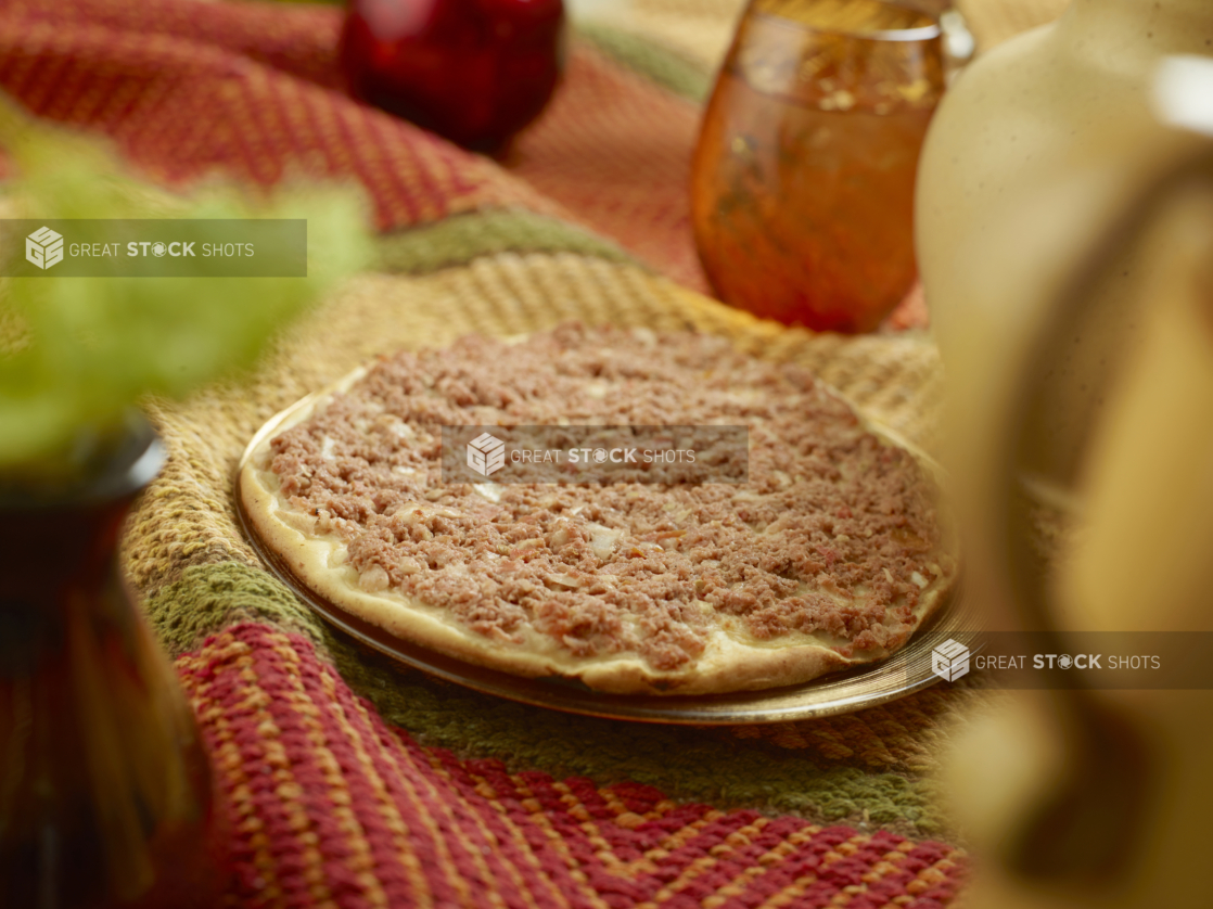 Lahmacun - Middle Eastern Baked Flatbread - with Minced Meat, Vegetables, Herbs and Spice Topping on a Colourful Woven Table Cloth in an Indoor Setting