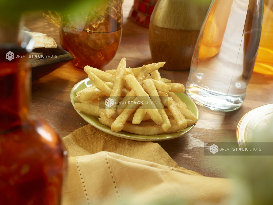 Small Ceramic Green Dish of Crispy Golden French Fries with a Yellow Napkin on a Wooden Table in an Indoor Setting