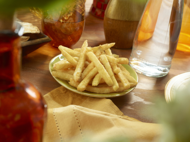 Small Ceramic Green Dish of Crispy Golden French Fries with a Yellow Napkin on a Wooden Table in an Indoor Setting