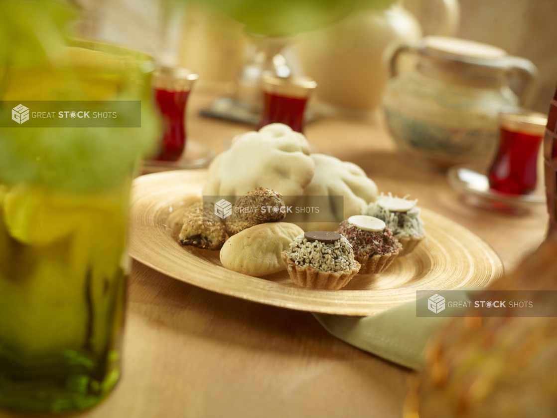 Assorted Middle Eastern Date-Filled Cookies and Mini Phyllo Baklava Cups on a Round Ceramic Dish on a Wooden Table in an Indoor Setting