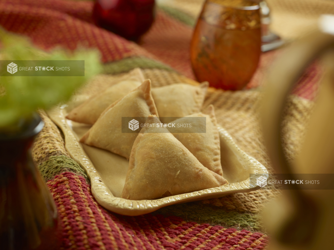 Fried Potato and Peas Samosas on a Rectangular Ceramic Plate on a Colourful Woven Table Cloth in an Indoor Setting