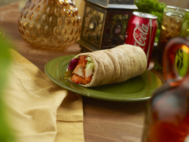 BBQ Chicken Kebab Pita Wrap with Pickled Veggies and Fresh Vegetables on a Round Ceramic Dish with a Can of Coke on a Wooden Table in an Indoor Setting