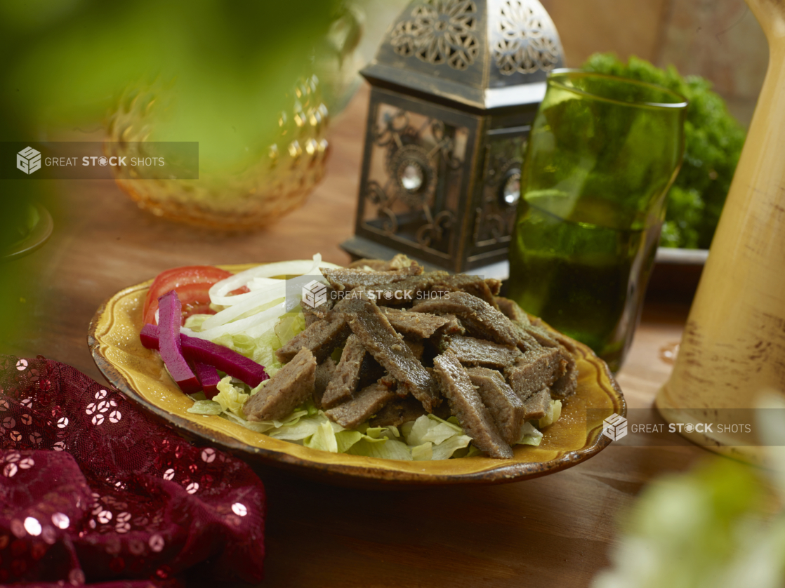 Gyro Salad with Shredded Lettuce, Sliced White Onions, Sliced Tomatoes and Picked Veggies in a Ceramic Dish on a Wooden Table in an Indoor Setting