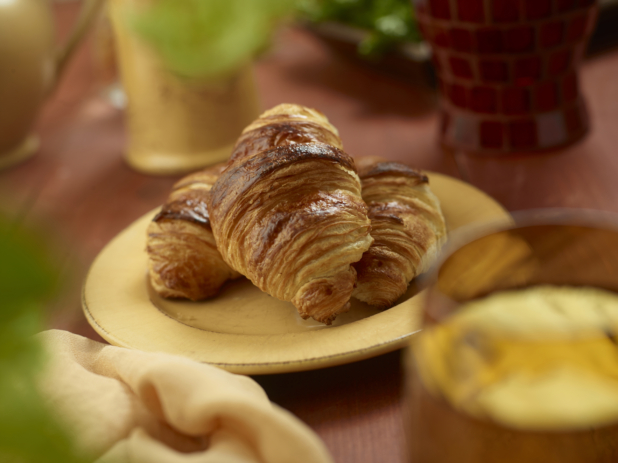A Trio of Fresh Baked Butter Croissants on a Round Yellow Plate on a Wooden Table in an Indoor Setting