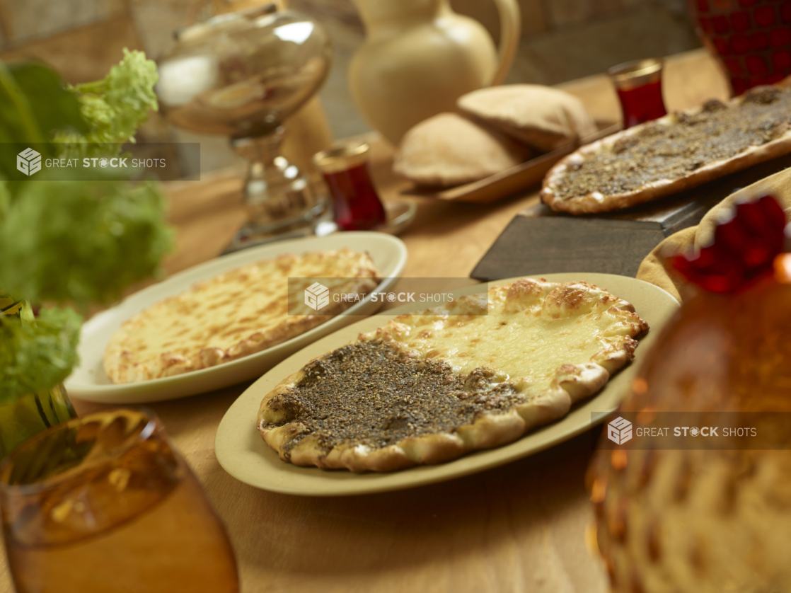 Middle Eastern Style Flatbreads with Cheese and Za'atar Spice Toppings on Round Dishes on a Wooden Table in an Indoor Setting