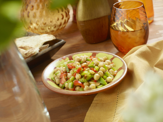 Chick Pea and Green and Red Pepper Salad in a Colourful Ceramic Dish with a Yellow Napkin on a Wooden Table in an Indoor Setting