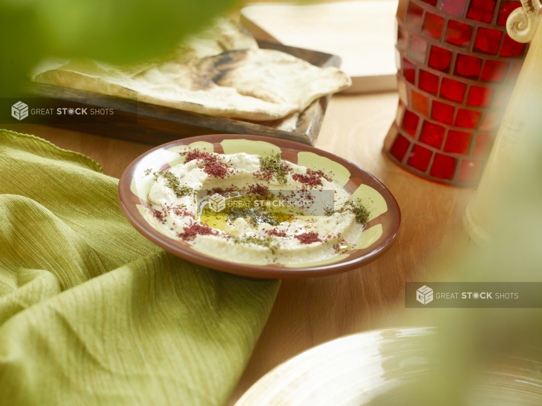 Middle Eastern Baba Ghanoush with Olive Oil and Spices and Pita Bread on a Wooden Table with a Red Mosaic Vase and Green Table Cloth