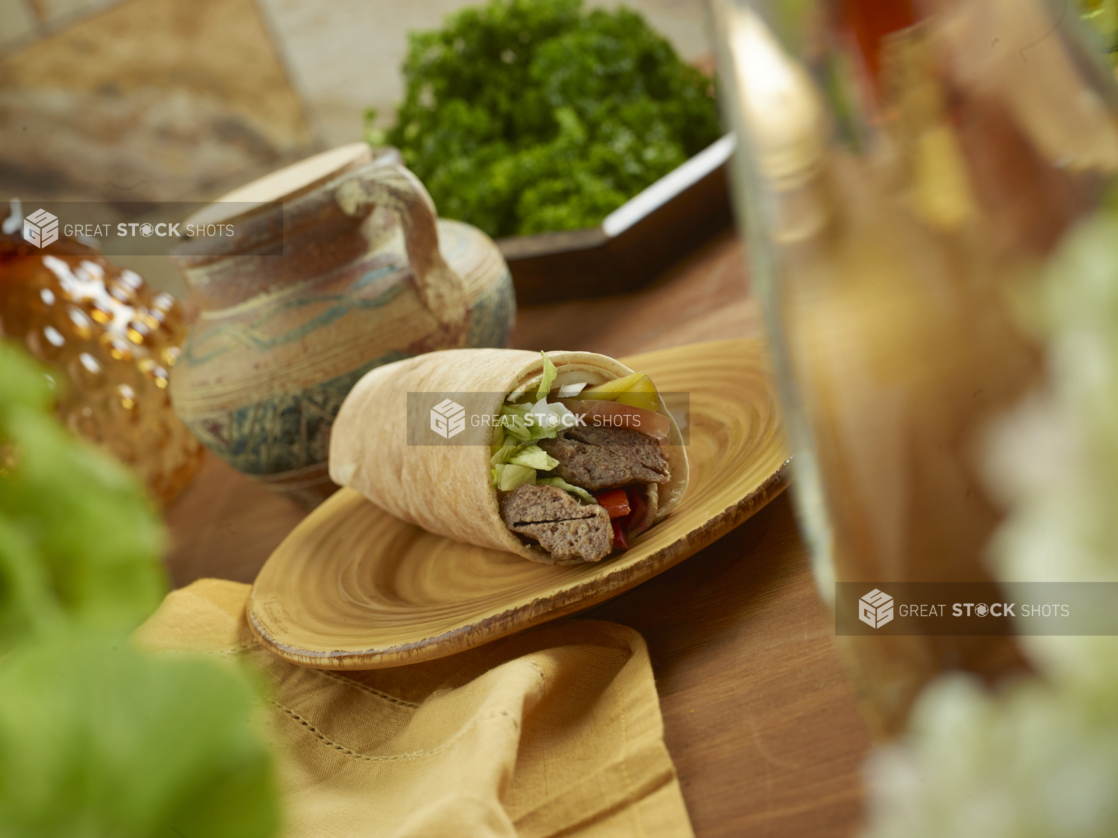 Beef Kebab Pita Wrap with Pickled Veggies and Fresh Vegetables on a Round Ceramic Dish on a Wooden Table in an Indoor Setting