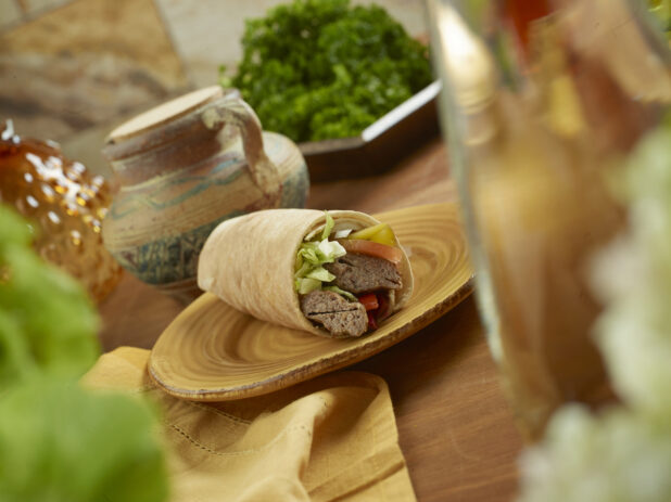 Beef Kebab Pita Wrap with Pickled Veggies and Fresh Vegetables on a Round Ceramic Dish on a Wooden Table in an Indoor Setting