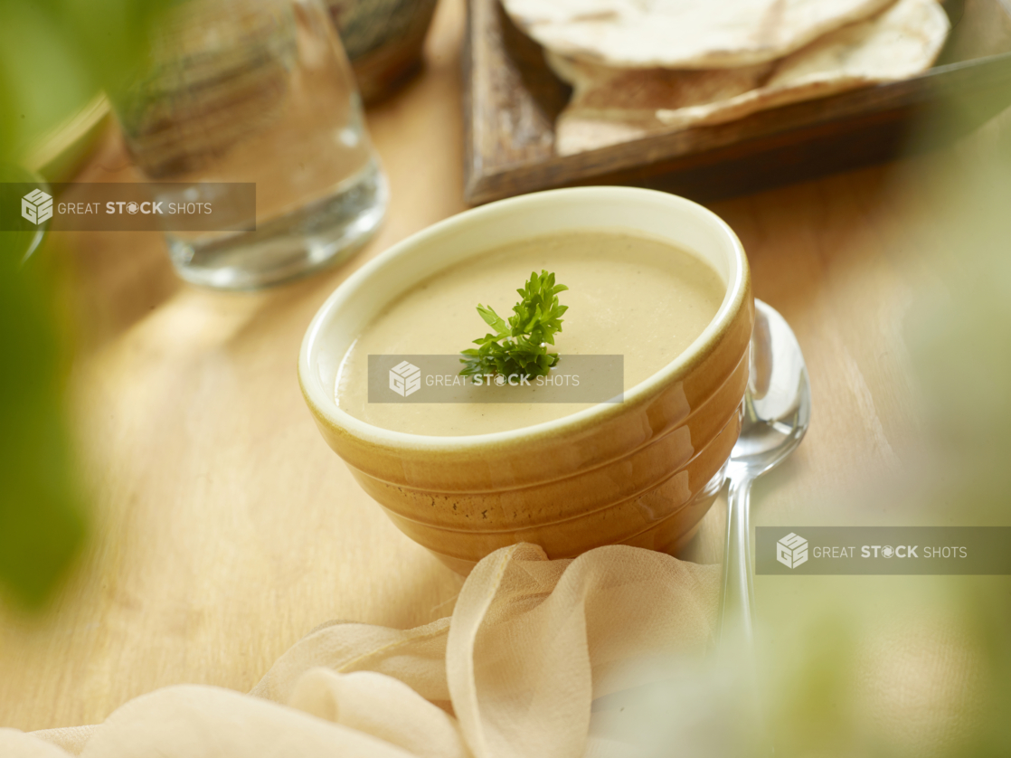 A Yellow Ceramic Bowl Filled with Hot Lentil Soup with Fresh Parsley Garnish on a Wooden Table in an Indoor Setting