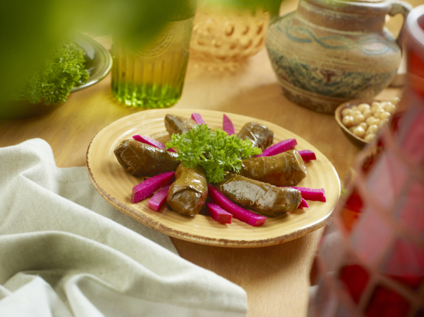 A Round Yellow Plate of Stuffed Marinated Lebanese Grape Leaves and Sliced Picked Red Beet on a Wooden Table in an Indoor Setting