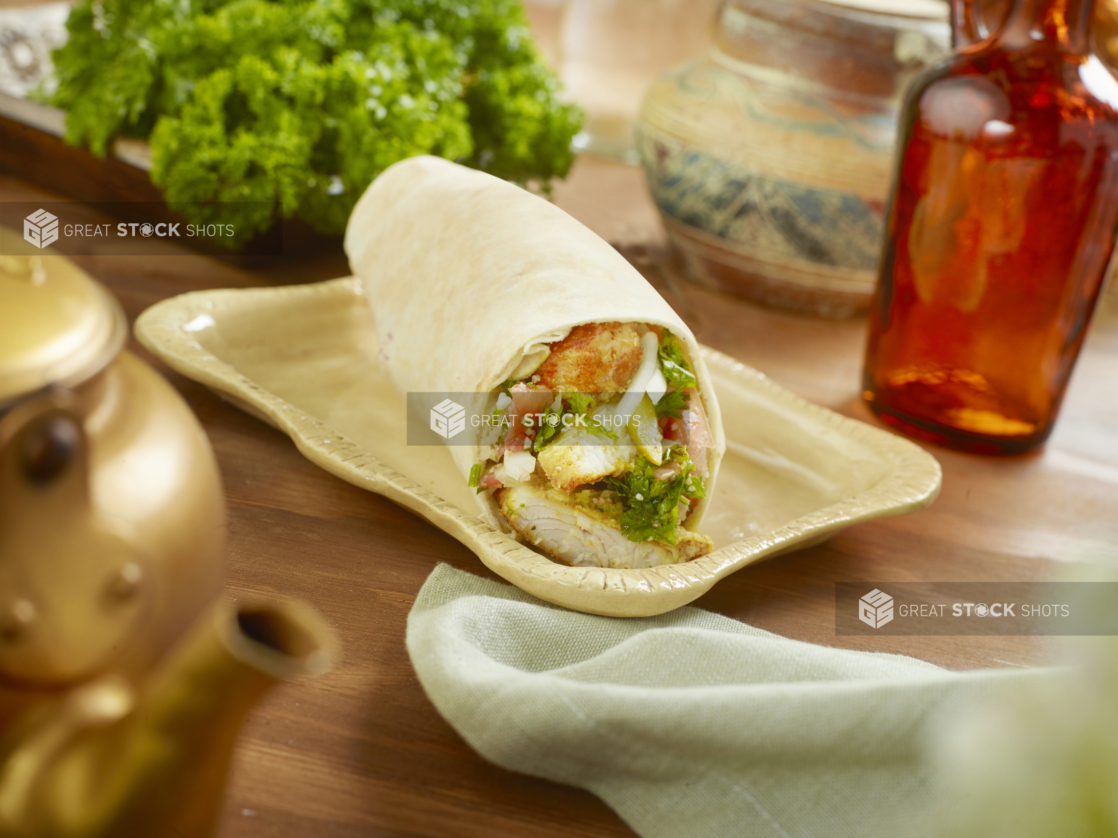 Fried Fish Pita Wrap with Tabbouleh on a Rectangular Ceramic Dish on a Wooden Table in an Indoor Setting