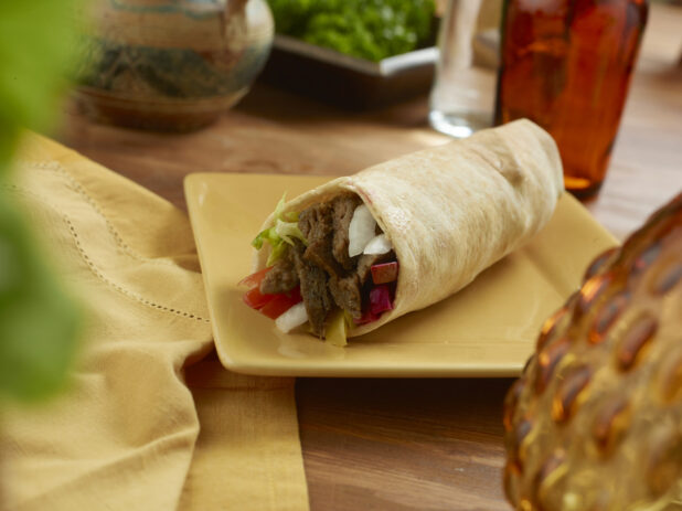 Beef Shawarma Pita Wrap with Pickled Veggies and Fresh Vegetables on a Rectangular Ceramic Dish on a Wooden Table in an Indoor Setting