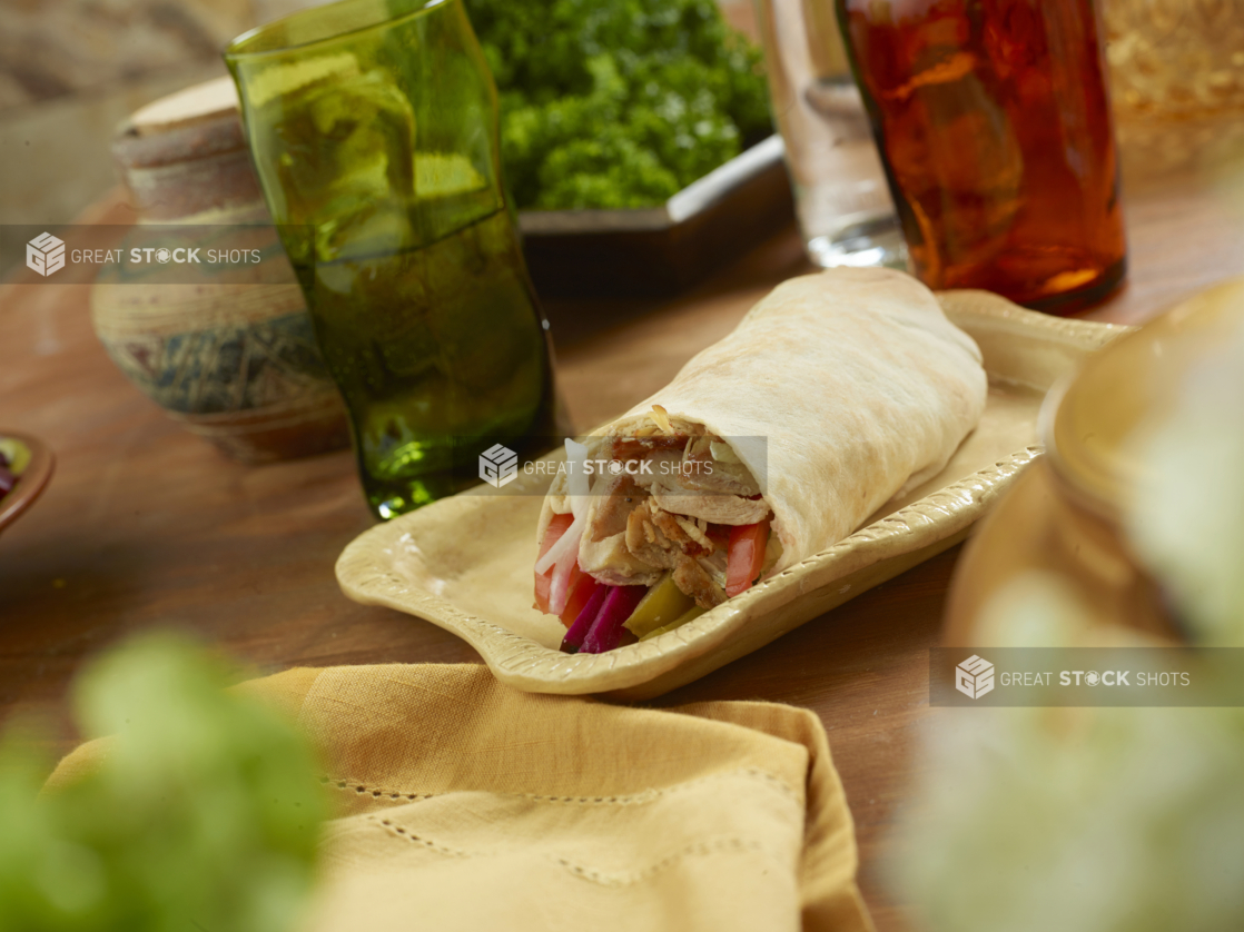 Chicken Shawarma Pita Wrap with Pickled Veggies and Fresh Vegetables on a Rectangular Ceramic Dish on a Wooden Table in an Indoor Setting