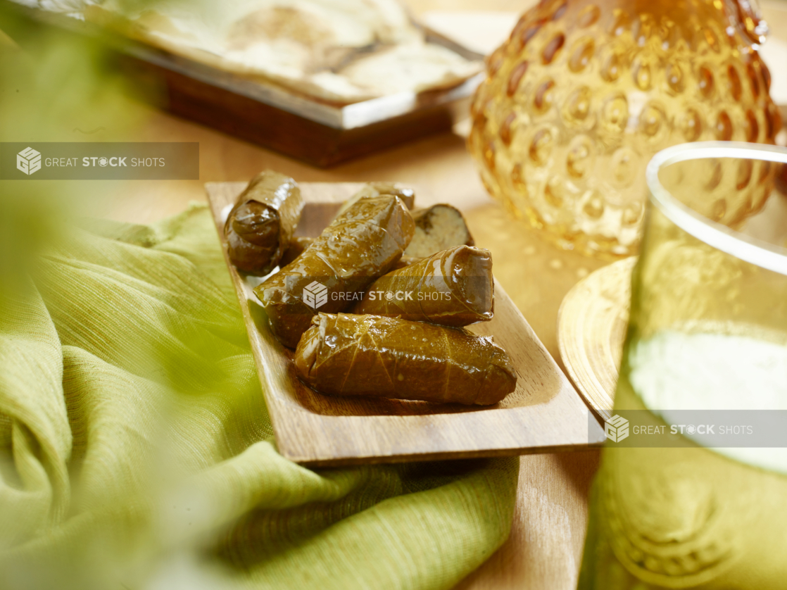 A Wooden Platter of Stuffed Marinated Lebanese Grape Leaves on a Green Table Cloth on a Wooden Table in an Indoor Setting