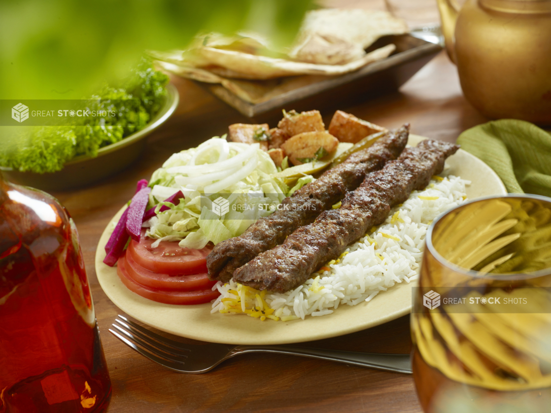 Beef Kebab Combo Dinner with a Garden Salad, Roasted Garlic Potatoes, Picked Veggies and White Rice in a Ceramic Dish on a Wooden Table in an Indoor Setting