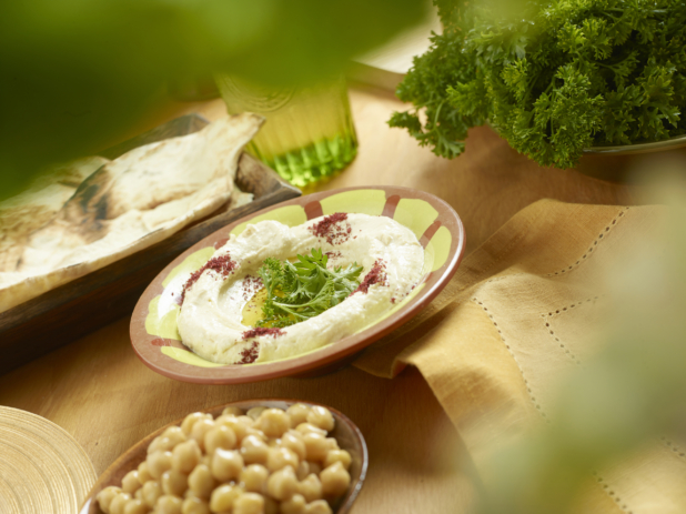 Middle Eastern Hummus with Olive Oil and Fresh Parsley Garnish on a Wooden Table with Parsley in the Background and Chick Peas in the Foreground