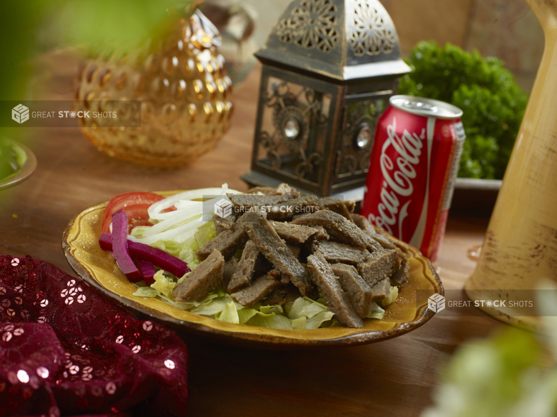 Gyro Salad with Shredded Lettuce, Sliced White Onions, Sliced Tomatoes and Picked Veggies in a Ceramic Dish with a Can of Coke on a Wooden Table in an Indoor Setting