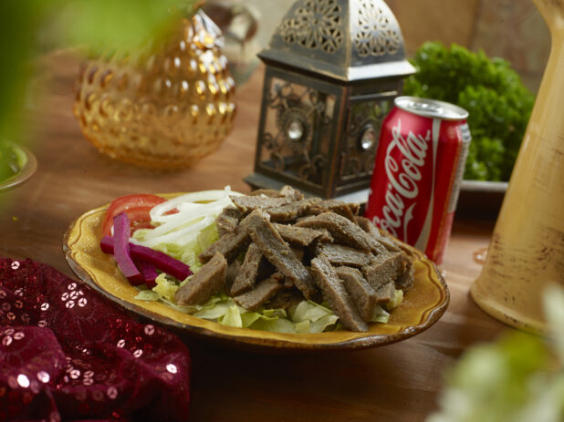 Gyro Salad with Shredded Lettuce, Sliced White Onions, Sliced Tomatoes and Picked Veggies in a Ceramic Dish with a Can of Coke on a Wooden Table in an Indoor Setting
