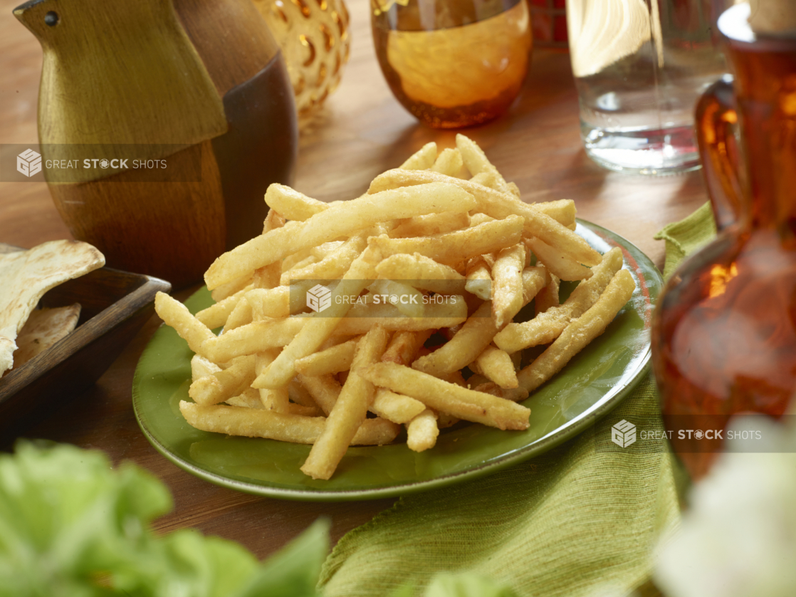 A Round Green Plate of Crispy Golden French Fries on a Green Napkin and Wooden Table in an Indoor Setting